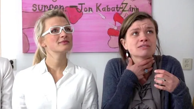 De sekszusjes zitten voor een schilderij met een ejaculerende penis en een gezicht, een van de sekszusjes grijpt naar haar keel.