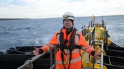 Een man in een oranje werkpak staat op een boot op zee.