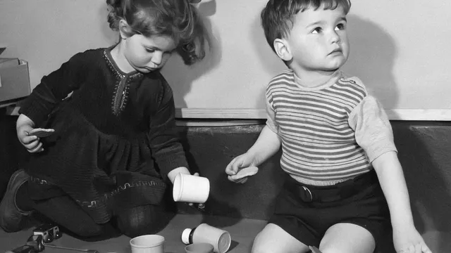 Een zwart-wit foto van twee jonge kinderen die op de grond met speelgoed spelen.
