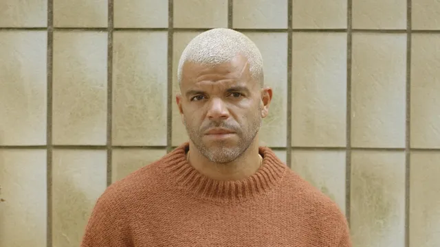 Sef met geblondeerd gemilimeterd haar en een trui met schedel aan voor een betegelde muur