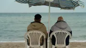 Twee mannen zitten op het strand op een stoel onder een parasol.