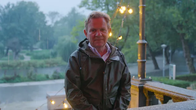 Man kijkt in camera onder een parasol met op de achtergrond regen.