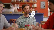 Een man met een kleurrijke blouse in een lunchtentje met bier