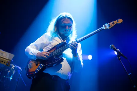 Bassist Bart Lubking van Antje Krook spelend tijdens een optreden in de Nobel in Leiden, onder mooie blauwe podiumverlichting