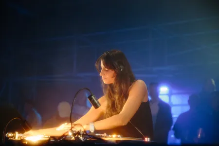 Vrouw achter de draaitafels staat geconcentreerd een plaat op te leggen