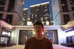Pete staat voor een gebouw met verlichting. De foto is in het donker genomen. Er valt een rood licht op de zijkant van Pete zijn hoofd.