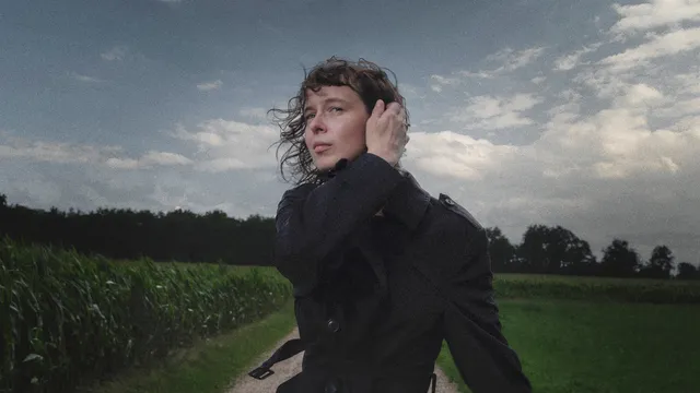 Vrouw haalt een hand door haar haar terwijl ze naast een maisveld staat