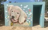Een betonnen schuilkelder, zo groot als een zeecontainer, met een muurschildering van een Golden Retriever-puppy met een halsband en vrolijk gekleurde wolkjes om hem heen.