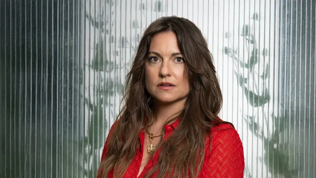 Foto van Eva Crutzen voor Zomergasten 2025 ze staat voor een semi groene muur en draagt een rode jurk