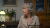 Een dame met grijs haar kijkt opzij in een woonkamer