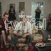 Een familie die in een huiskamer op banken zit en naar een televisie kijkt. Ook staat de tekst 100 jaar twijfelen in beeld.