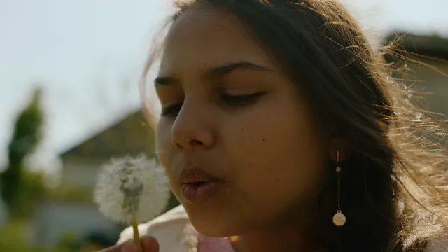 Meisje met donker haar in de zon blaast tegen een paardebloem