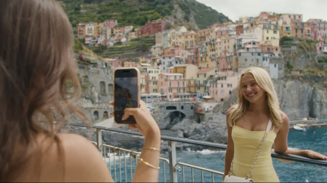 Een jonge vrouw poseert voor de smartphone-camera van een andere vrouw voor een zee bij een Italiaans kustdorpje.