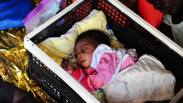 Een donkere baby ingewikkeld in dekens ligt in een plastic kratje