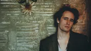 Een jonge man, Jeff Buckley, kijkt in de camera terwijl hij tegen een muur aanleunt.