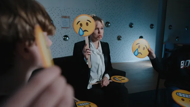 Een vrouw die verdrietig kijkt met een bordje in haar hand van een emoji die ook zielig kijkt
