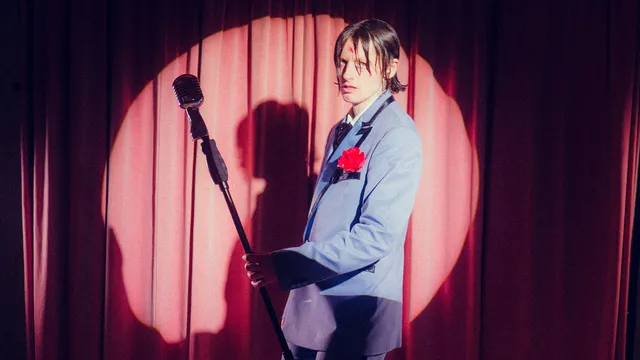 Elmer staat in de spotlight omringd door rozen voor een rood gordijn met een microfoon