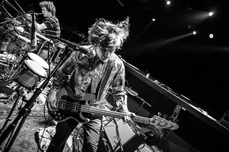 Foto van de basgitarist van Fellatio. Hij schudt zijn haren wild in het rond.
