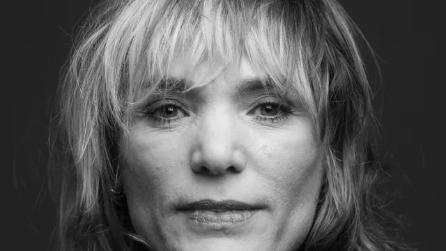 Zwart-wit foto van blonde vrouw, houdt haar handen op elkaar voor haar kin, draagt veel ringen.