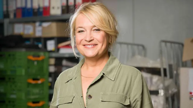 Een vrouw met blond haar en in een groene blouse tussen archiefkasten.