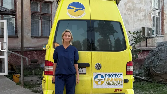 Frederiek Roukens staat in medische kleding voor een ambulance van Protect Ukraine.