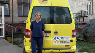 Frederiek Roukens staat in medische kleding voor een ambulance van Protect Ukraine.