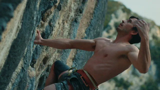 Een man zonder shirt die een berg aan het beklimmen is