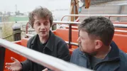 Twee mannen in rode bankjes van een schommelschip. Op de achtergrond de haven van Rotterdam.
