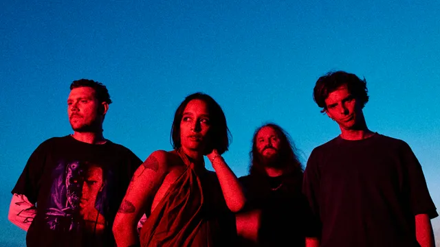 4 bandleden naast elkaar in rood licht met een donkerblauwe lucht