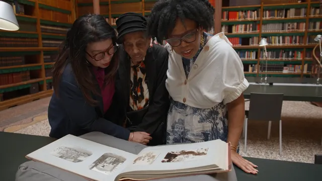 Drie vrouwen staan gebogen over een fotoalbum
