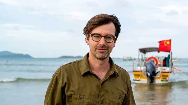 Ruben Terlou kijkend in de camera terwijl hij voor de zee staat