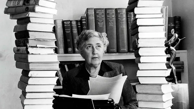 Mystery author and writer, Agatha Christie, pictured at her home, Winterbrook House in Wallingford, Berkshire, sitting behind her desk with books piled high, 1950.