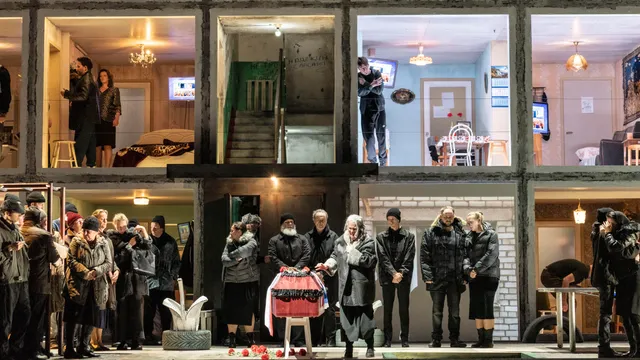 Verschillende mensen staan rondom een kist. Op de achtergrond zie je een dwarsdoorsnede van een flatgebouw. Het is een scene uit de opera Boris Godoenov