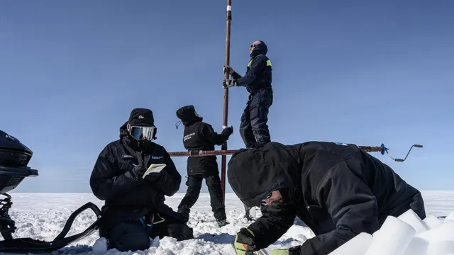 Op een witte ijsvlakte, oostelijk Antarctica, staan en zitten vier wetenschappers die onderzoek doen naar het ijs. Ze zijn ingepakt in dikke, zwarte outdoorkleding. Twee van hen houden een paal omhoog op de achtergrond, het lijkt een boor te zijn om het ijs omhoog te halen. Op de voorgrond zitten de andere twee wetenschappers, de ene schrijft in een logboek en de ander graaft in de sneeuw.