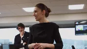 Een vrouw met haar haar in een knot staat glimlachend in een vergaderruimte en lijkt een gesprek of presentatie te leiden.