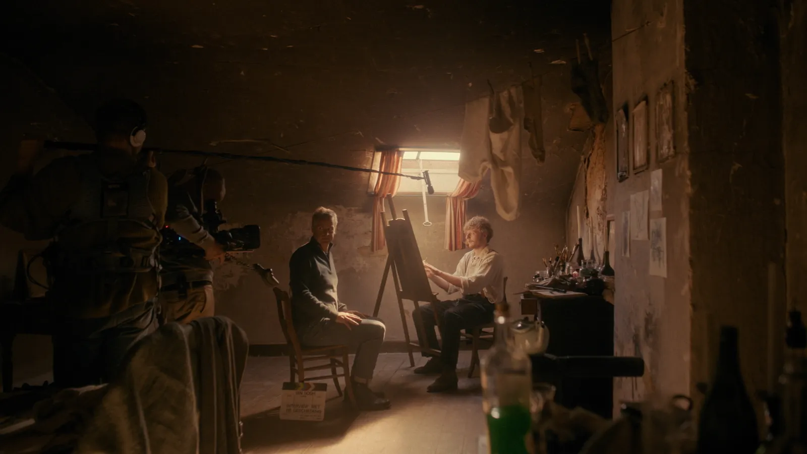 Filmopname in donker atelier met acteur als schilder en camerateam.