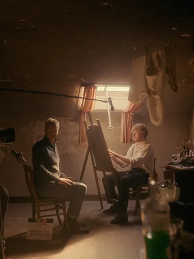 Filmopname in donker atelier met acteur als schilder en camerateam.