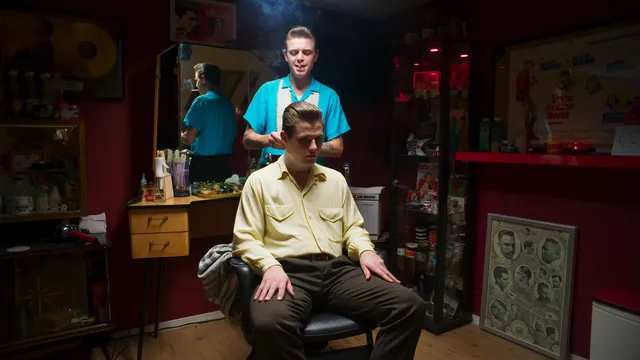 Een kapper met een sigaret in zijn mond knipt het haar van een man in een kappersstoel