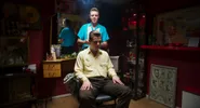 Een kapper met een sigaret in zijn mond knipt het haar van een man in een kappersstoel