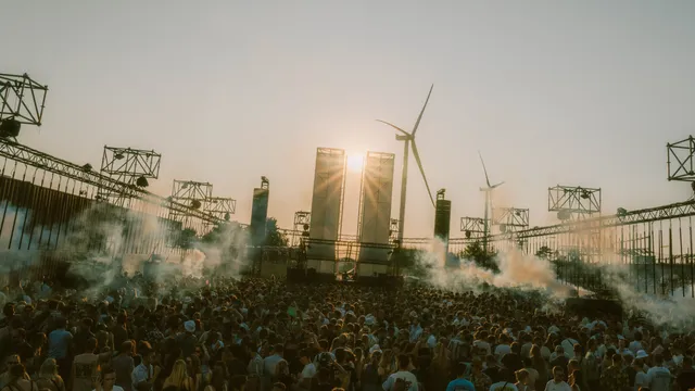 Festivalterrein met ondergaande zon en twee windmolens