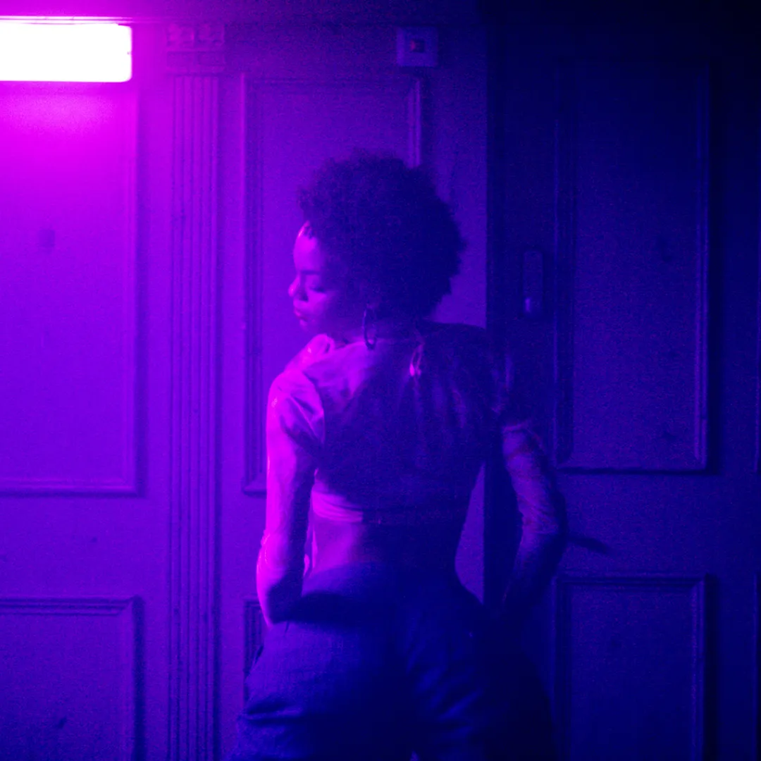 Vrouw staat in een neon verlichte club met de rug naar ons toe te dansen.