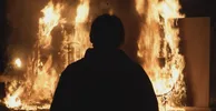 Een silhouet staat voor vlammen. Er staan voorwerpen in de fik.