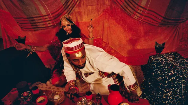 Sudanese-Dutch artist sitting in tent in traditional clothing in front of a table with tea and lights