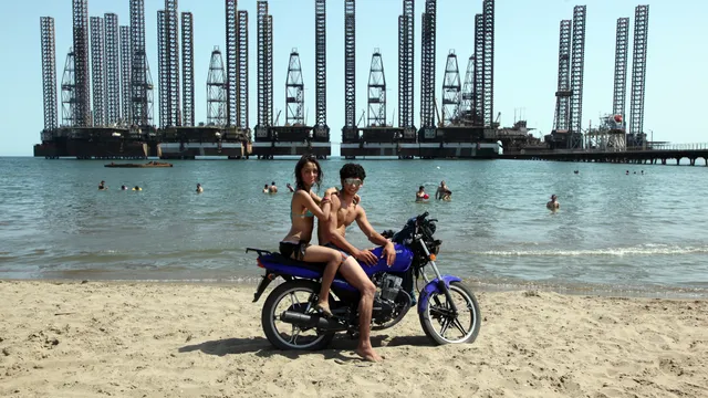 Jong stel op het strand vlakbij Bibi Heybat, met op de achtergrond een olieplatform uit vervlogen tijden