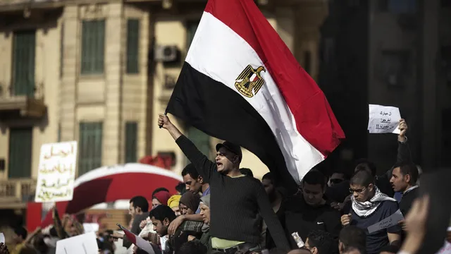 Een man houdt de Egyptische vlag omhoog om het Tahrirplein. Om hem heen staan meer betogers.
