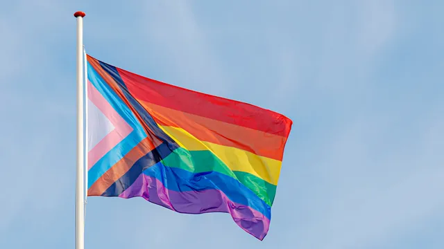 Progress pride flag (new design of rainbow flag) waving in the air with blue clear sky, Celebration of gay pride, The symbol of lesbian, gay, bisexual and transgender, LGBTQ community in Netherlands.