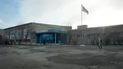 Foto van een grijs gebouw met lichtblauwe ingang, daarvoor staat een vlaggenmast waaraan de Russische vlag wappert