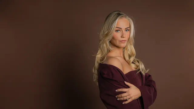 Marijn is een blonde vrouw met blauwe ogen die serieus naar de camera kijkt tegen een bruine achtergrond.