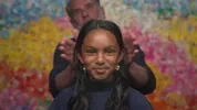 Darshni zit in de kappersstoel, met een glimlach kijkt ze de camera in