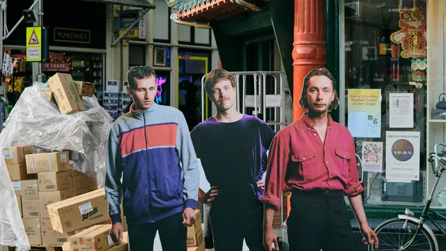 de drie bandleden van the homesick staan op een kartonnen bord afgebeeld op de zeedijk in Amsterdam